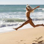 Carefree naked young woman jumping at beach against sea stock photo