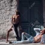 Woman With Naked Breasts Man With Nude Torso Lies Outdoor. Sexy Couple Undressing Under Sunlight With Ancient Rocky Wall And Old Door On Background. Passion And Erotic Concept. Couple Enjoys Nudity. Stock