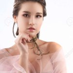 Beautiful young big breast asian girl wearing a pink veil on her naked shoulders and a choker on her neck sensually touches her face and neck. Isolated on white. Smooth healthy skin.